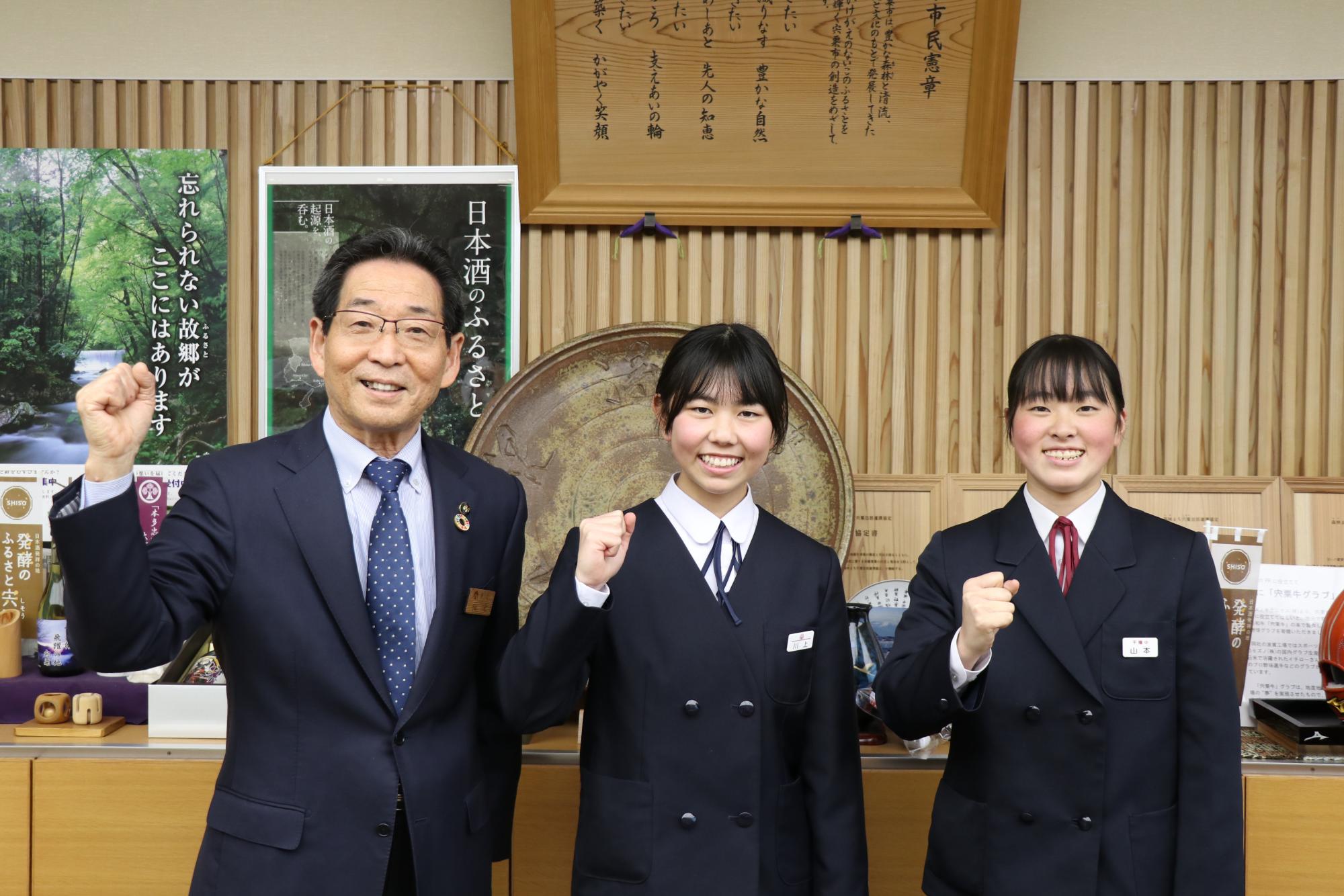 市長室で川上さん（中）と山本さん（右）が市長と横一列に並び、ガッツポーズをしている写真