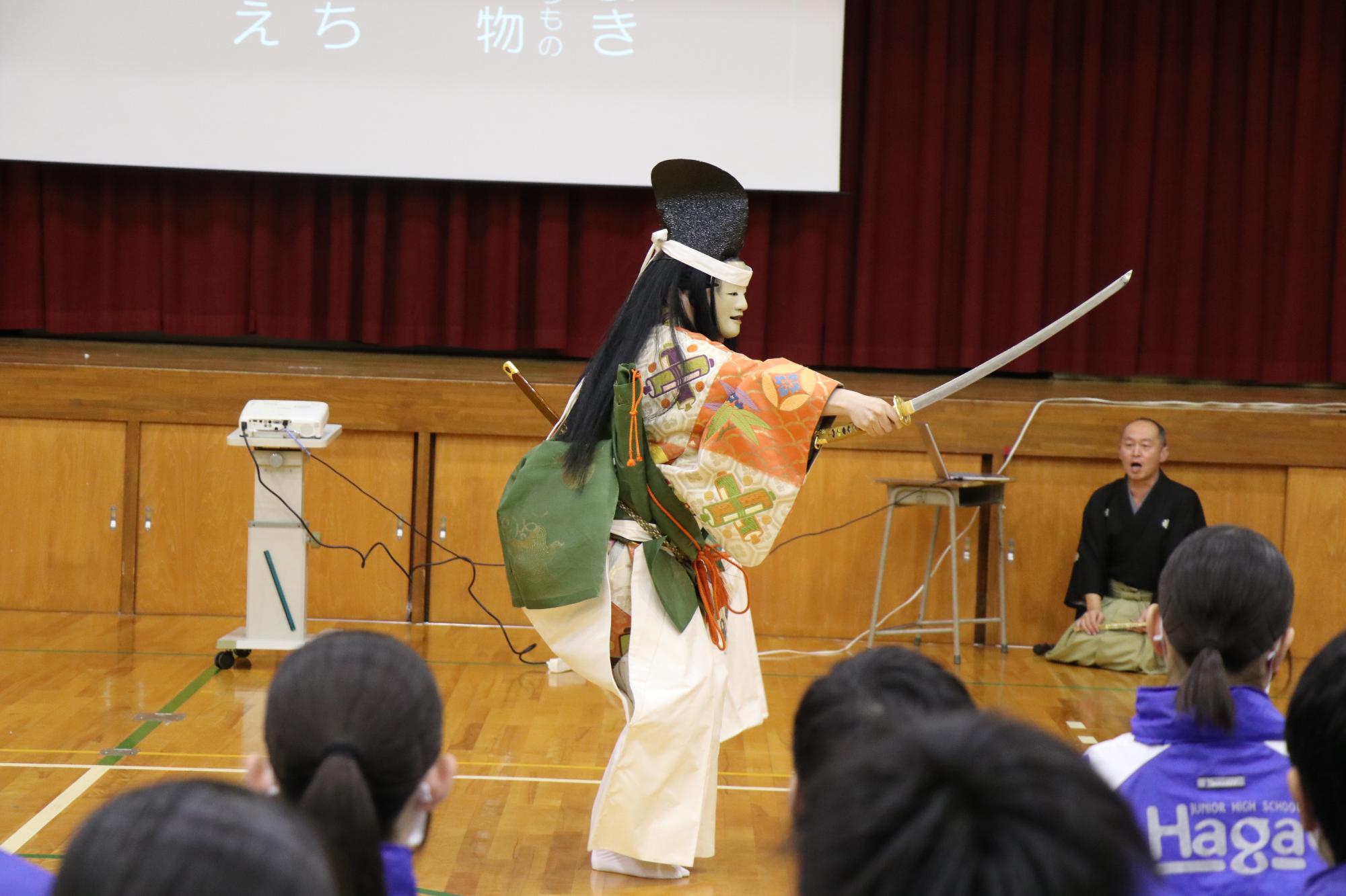 波賀中学校の体育館で能が演じられ、生徒たちが座って鑑賞している写真