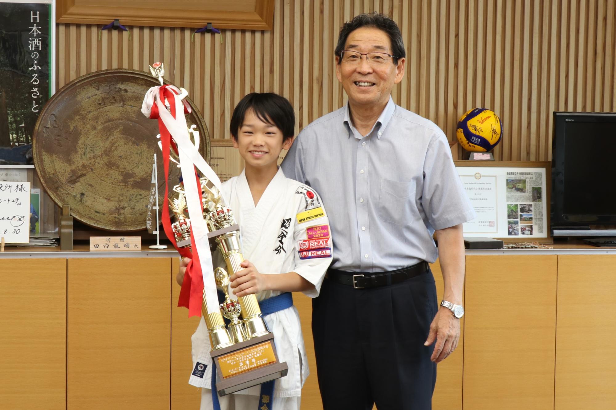 トロフィーを手に持った藤田さんと福元市長が並んで記念撮影した写真