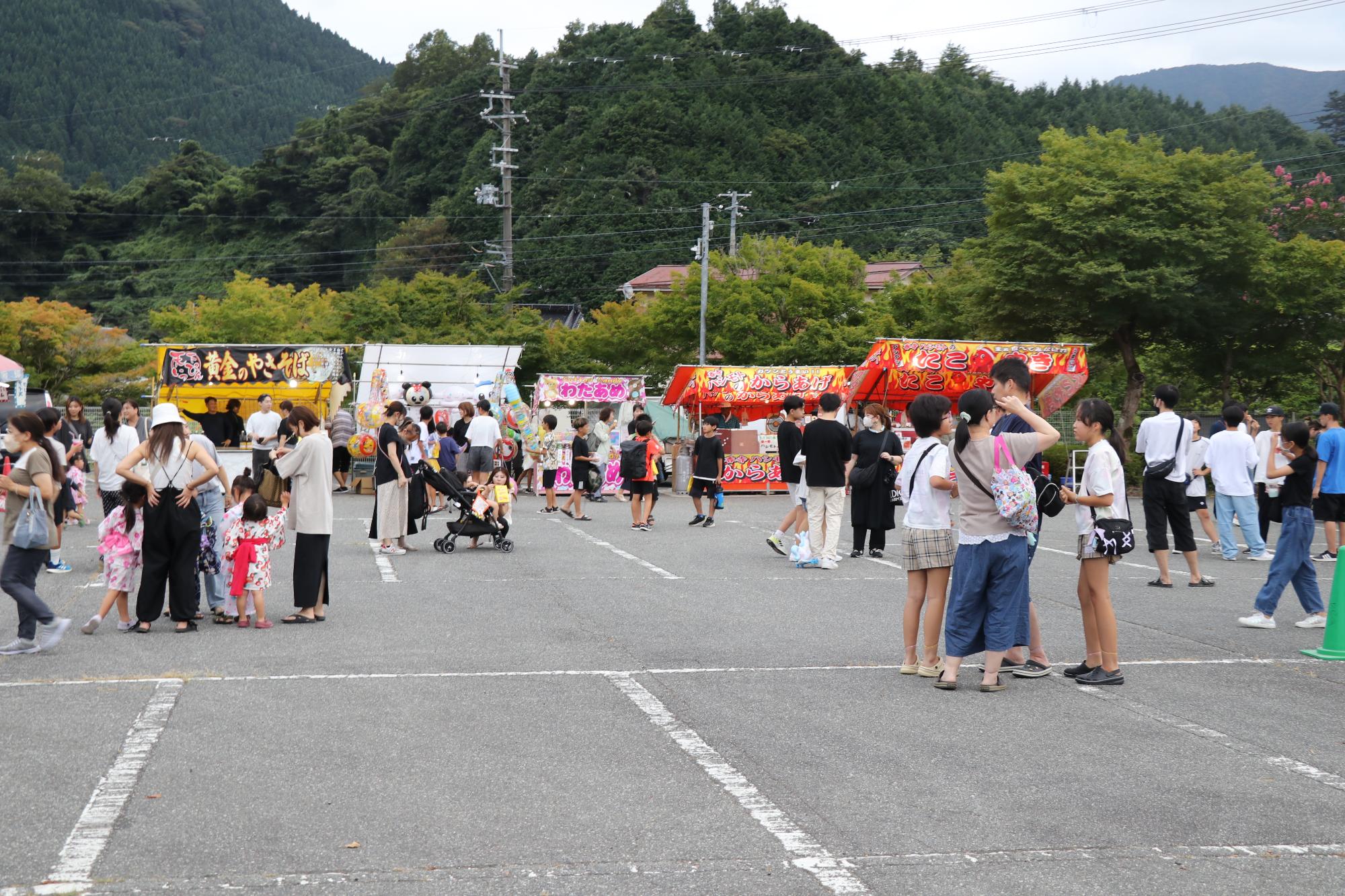 食べ物などの夜店が出店し、会場内のいたるところで地域住民の輪ができている様子の写真