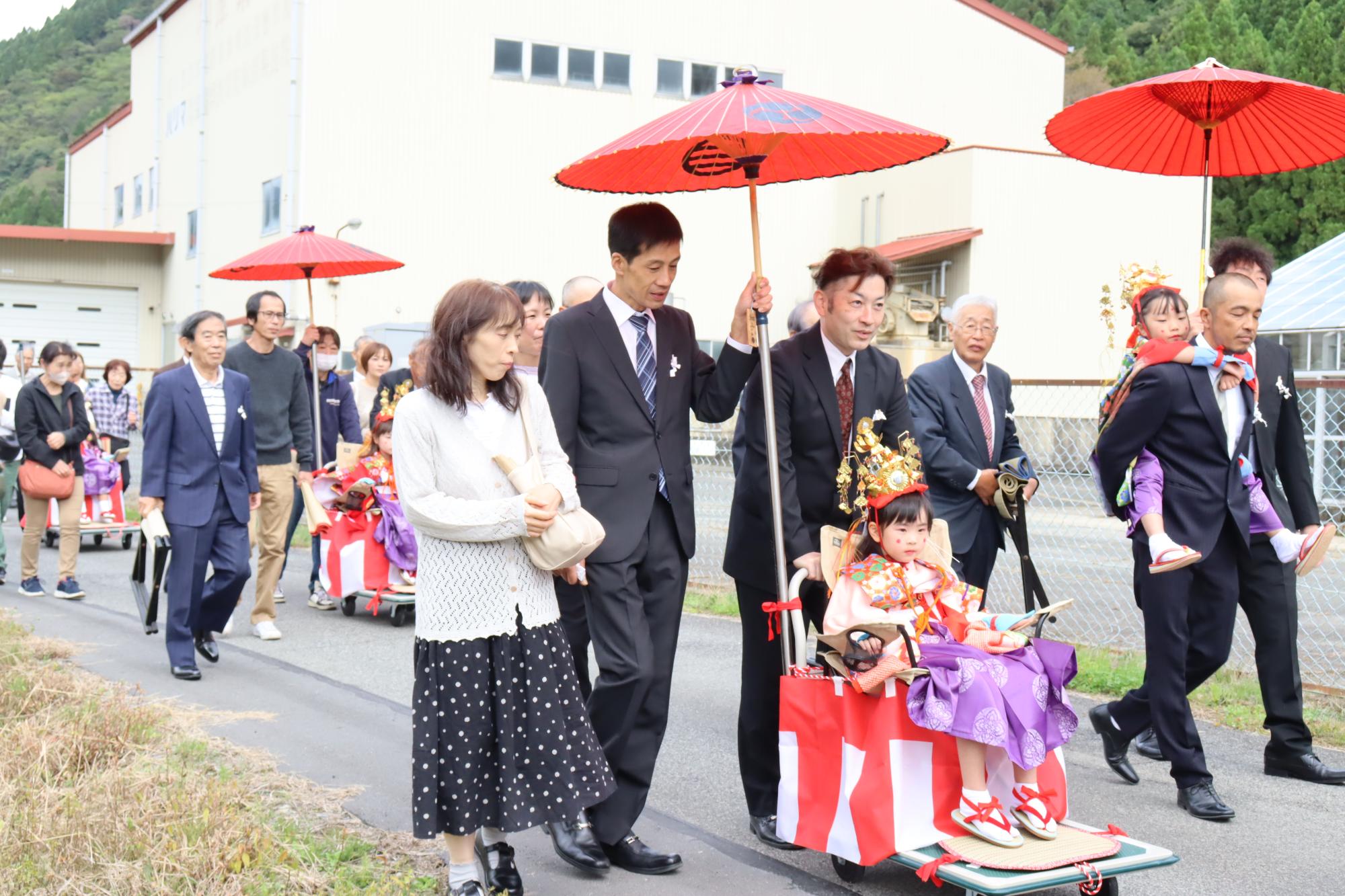 少女神子が手押し車や大人の背に乗って移動している写真