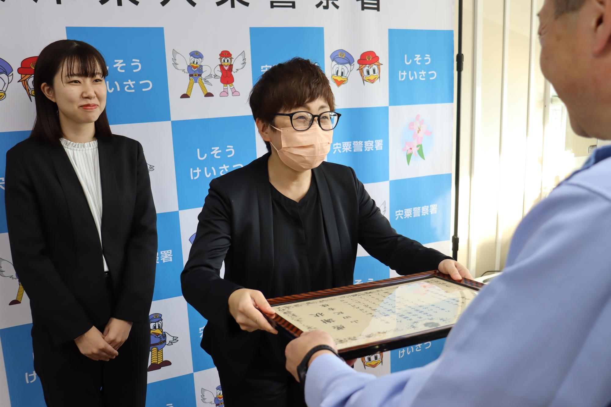 宍粟警察署の三浦保志署長から感謝状を受け取る山田さんと、その様子を後ろから笑顔で高田さんが見ている写真