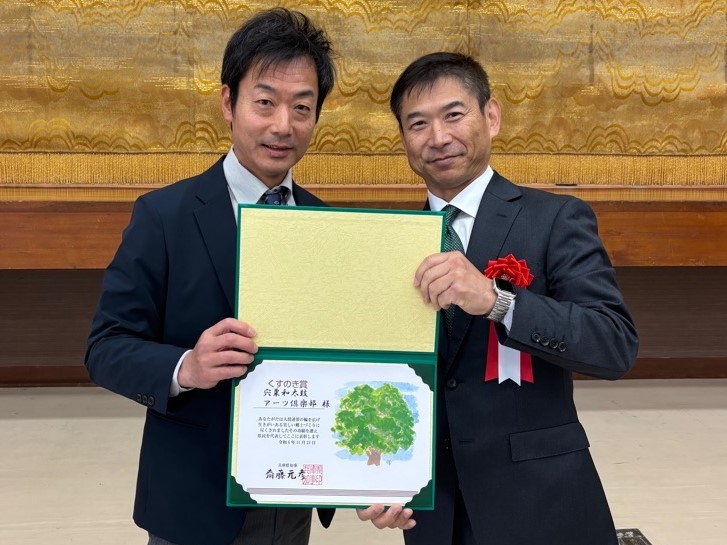 宍粟和太鼓アーツ俱楽部代表の志水昭彦さん（右）と副代表の藤永さんの2人がくすのき賞の賞状を両側から手でもって正面を向いている写真