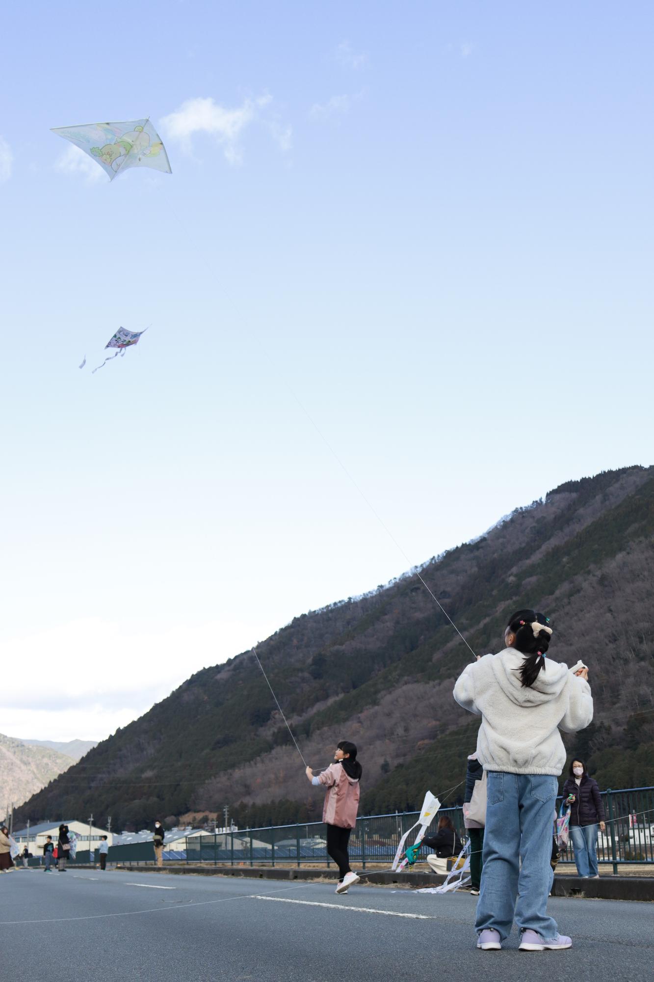 空に揚がった凧が落ちないように女の子が糸をゆるめたり引っ張ったりしている写真