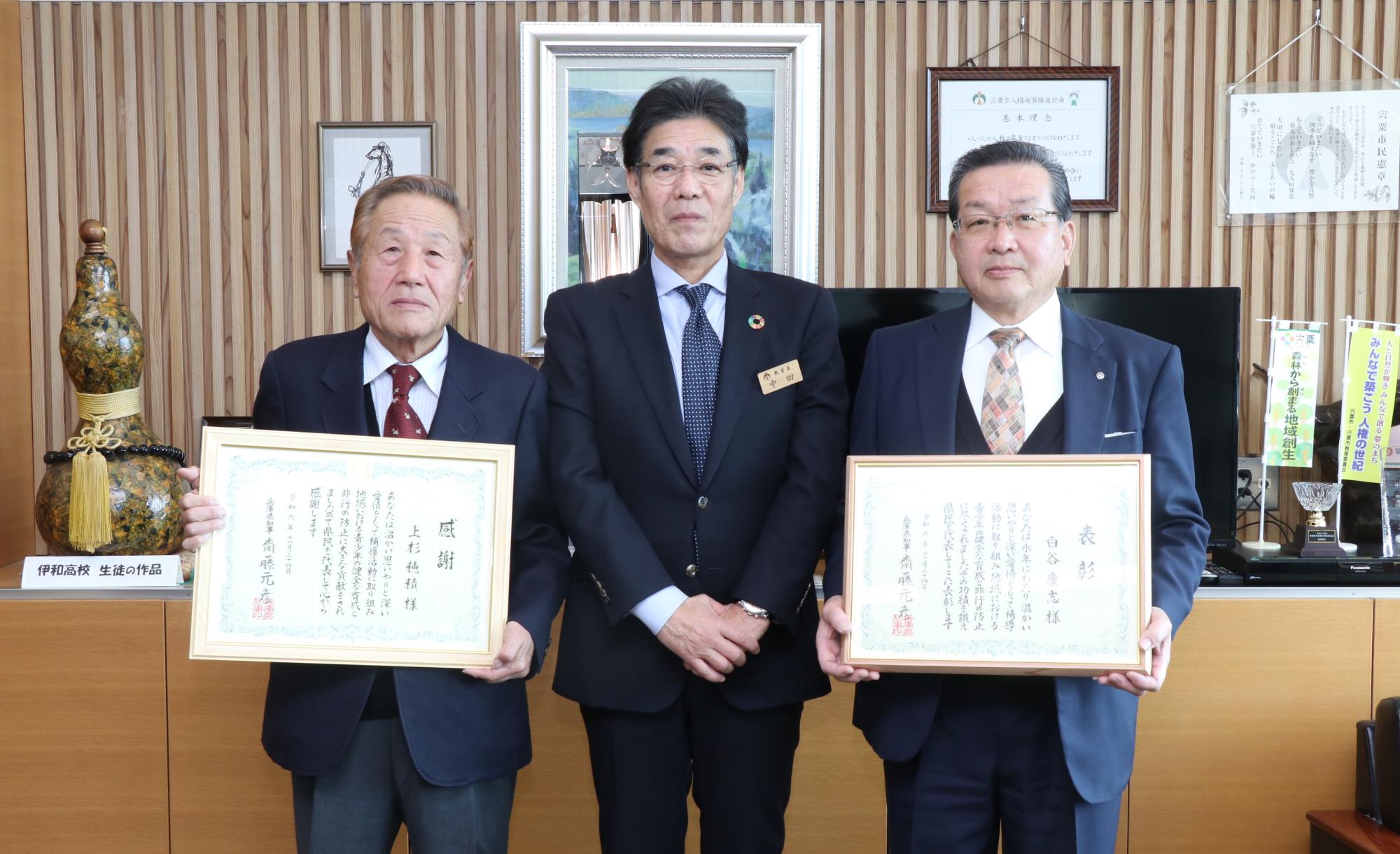 宍粟市教育長（中央）、賞状の入った額を手にもった白谷康志さん（右）と上杉穂積さんが並んで立っている写真
