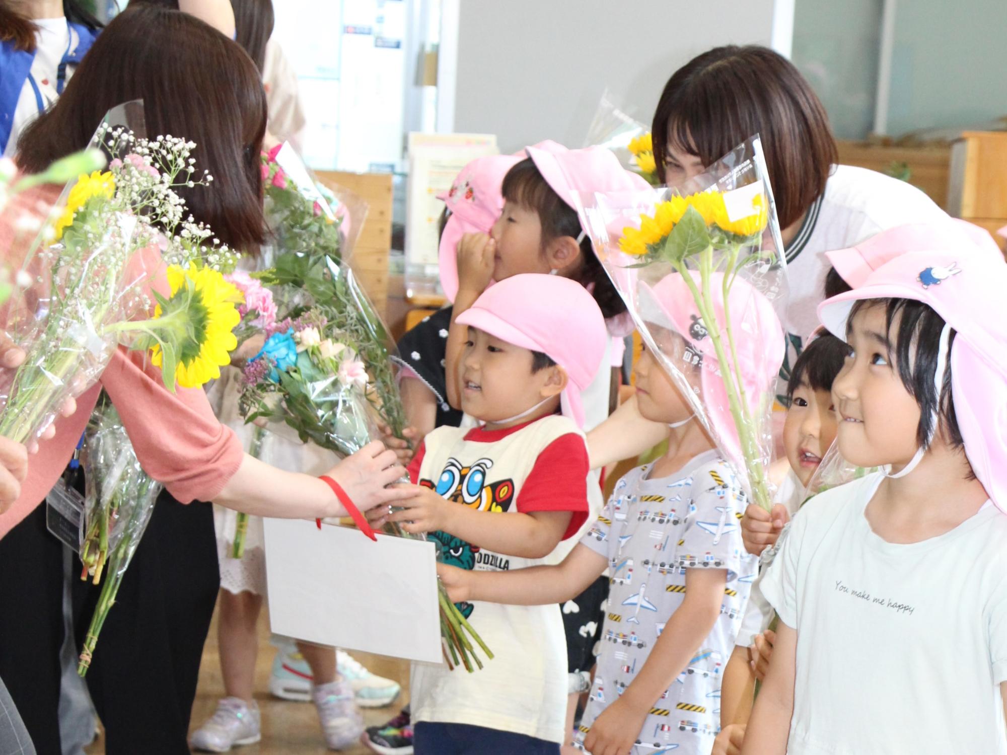花の日に市役所を訪れ市職員に花を手渡す山崎聖旨保育園の園児たちの写真