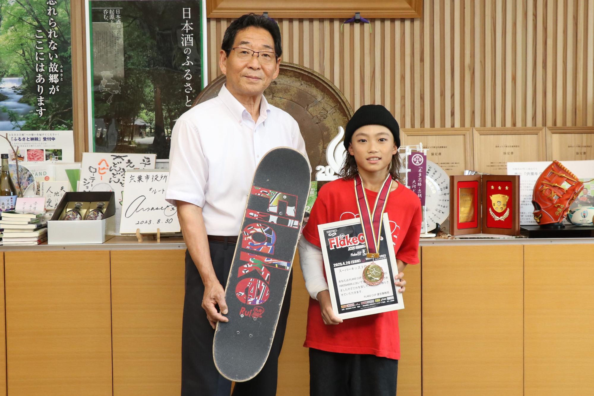 スケボーを持っている市長と予選の賞状とメダルをもった谷河さん