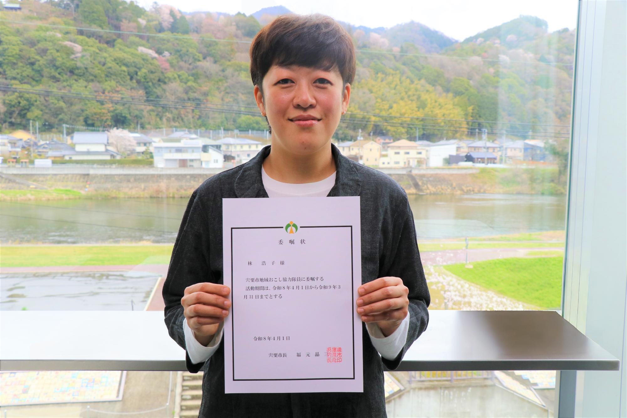林浩子さんが委嘱状を持って微笑んでいる様子
