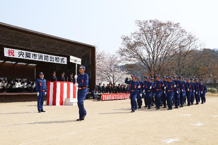 紺色の作業服を着た消防団員がグラウンドで行進をしている写真