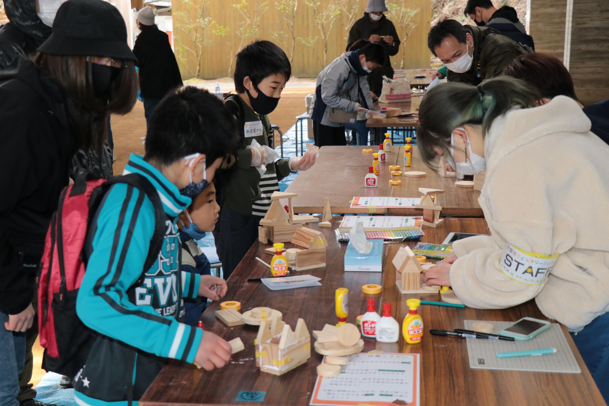 学遊館の会場で木工の家づくりを体験する子どもとそれを教える京都芸術大学の学生の写真