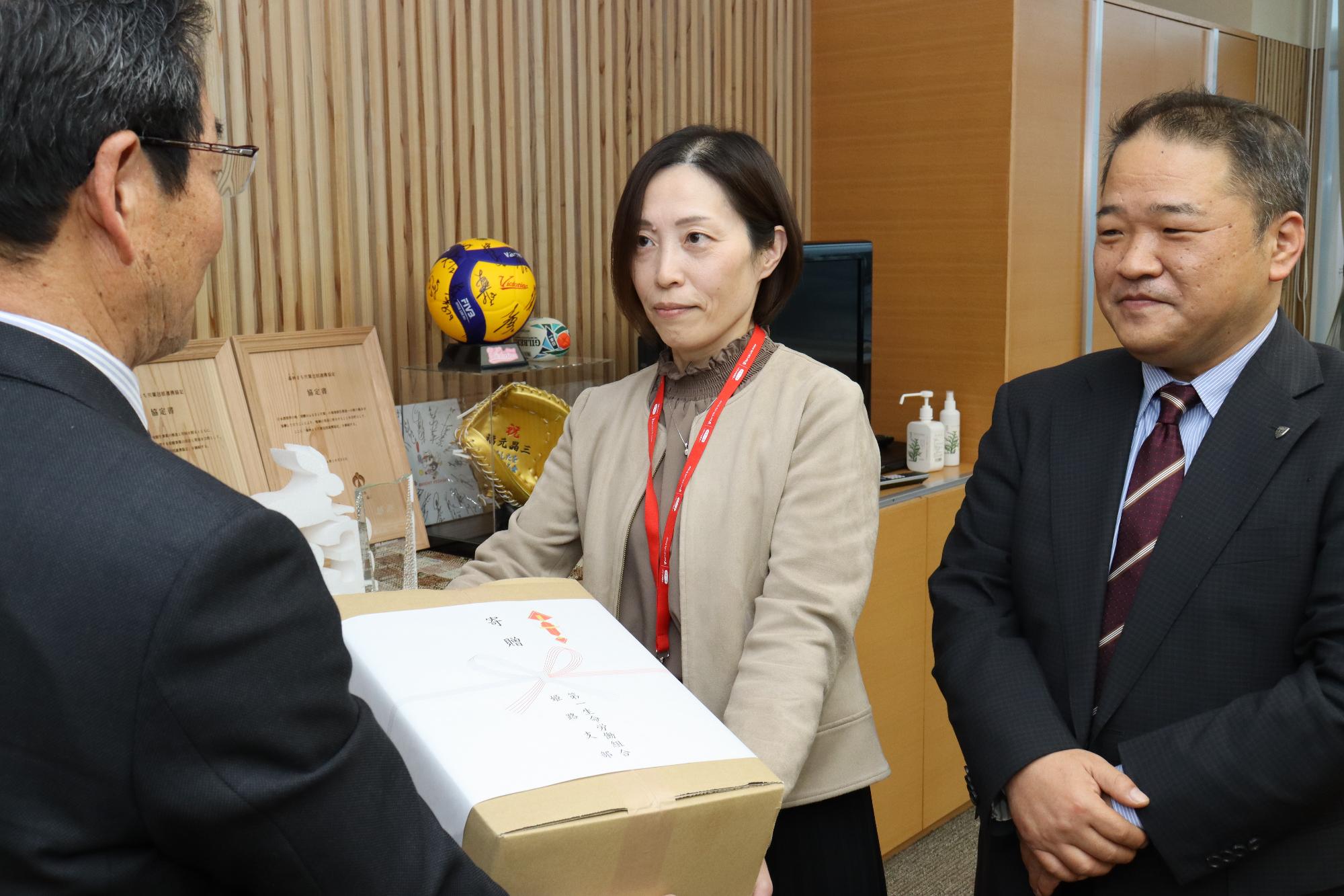 第一生命の小野さんが寄贈する絵本の入った箱を福元市長に手渡している写真