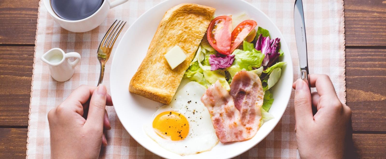 バターののったトーストに野菜サラダとカリカリベーコンが添えられた朝ごはんの写真