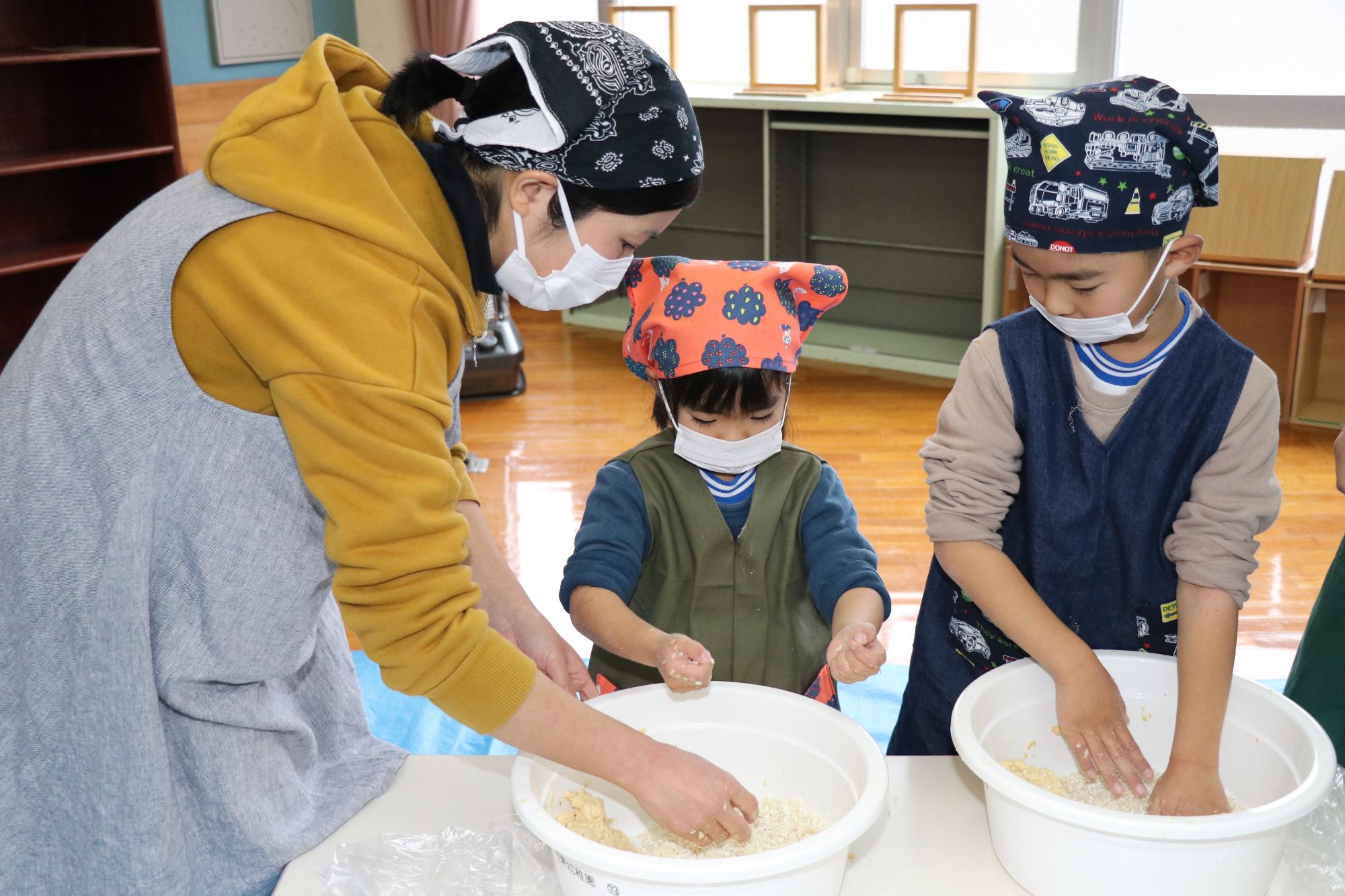 河東幼稚園で大豆を手でつぶしながらみその仕込みをしている親子の写真