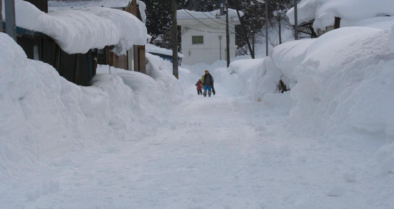 真っ白な雪に覆われた市道を歩く男性と女の子の写真