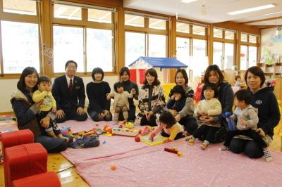ピンクのカーペットが敷いてある子供の遊ぶスペースで撮った7組の母子と市長の記念写真