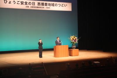 大きなステージ上の演壇で手話通訳者とともにスピーチをする市長の写真