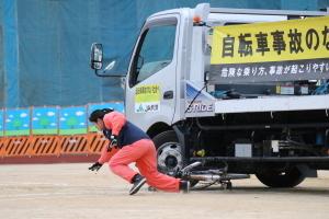 自転車乗車中にトラックとぶつかるスタントをするサーモンピンクの運動着を着たスタントマンの写真