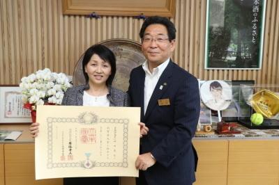 瑞宝単光章（児童福祉功労）受章証を持つ仲田真弓先生と市長の写真