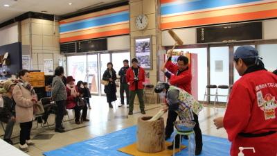 駅構内で行われるきてーなしそう餅祭りで赤い法被をきて餅をつく市長と周りに集まった通行人らの写真