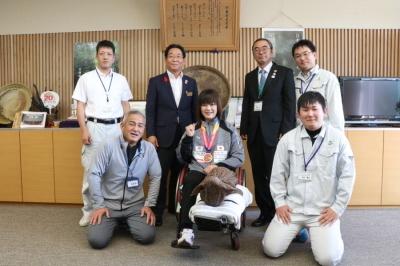 左足が前にまっすぐ伸びた状態で車椅子に座る西家さんと市役所職員達の写真