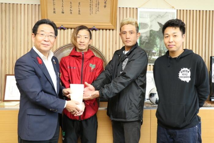 観光大使のロックミュージシャンの三人が義援金を市長に寄贈している写真