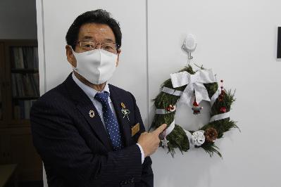 福元市長が白いリボンで飾られたクリスマスリースと並んでいる写真