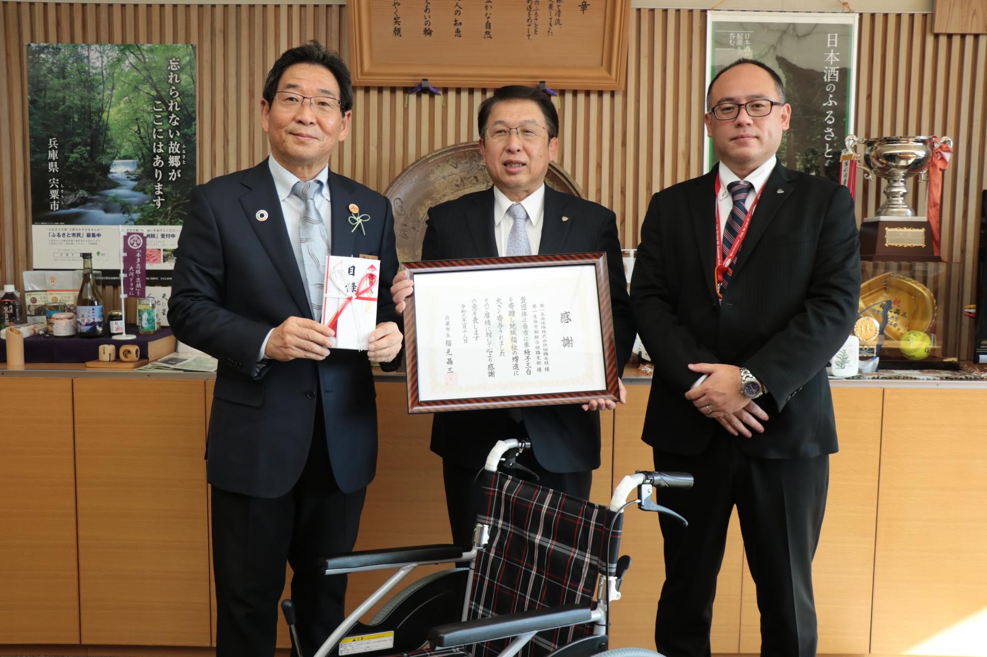 車椅子1台を中心に、左から福元市長、第一生命保険姫路支社支社長の池本昌永さん、営業部長の新谷喜一さんの写真