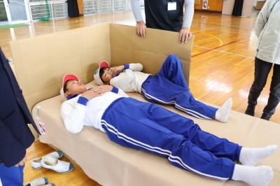 設置したシングルベッドサイズのダンボールベッドに小学生2人が並んで寝ている写真