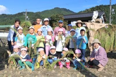 刈り取った稲を持っている子どもたちとかかしの記念写真