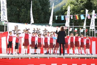 赤いユニフォームを着た合唱団がステージ上で歌っている写真