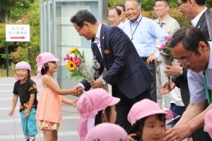 ピンクの帽子と淡いオレンジの服を着た園児からひまわりなどの花束を受け取る市長の写真