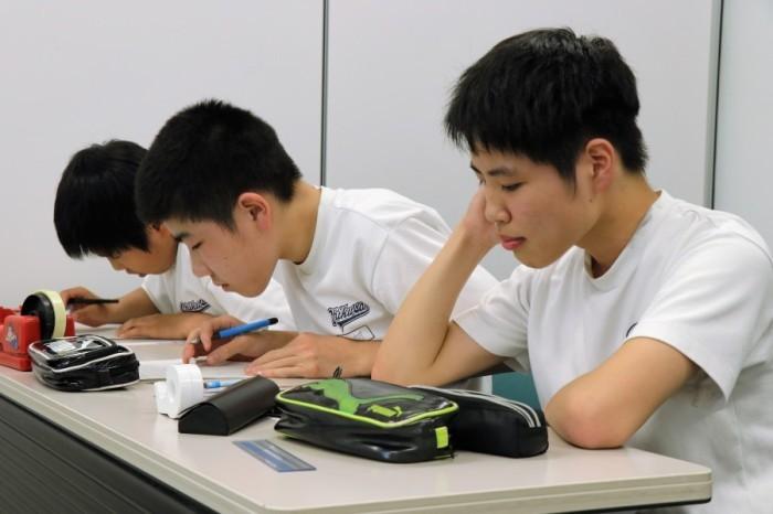 白いおそろいのTシャツを着た3人の中学生が机に向かい問題をといている写真