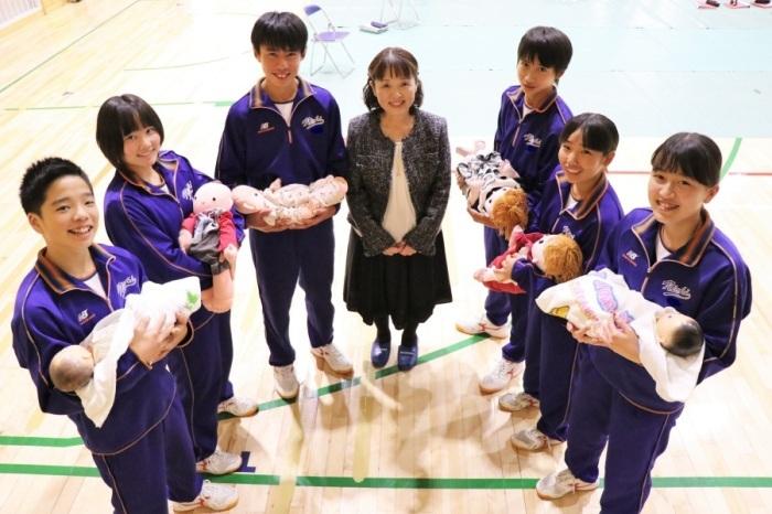 助産師の齊藤さんを中心に、人形の赤ちゃんを笑顔で抱いている中学生たちの写真