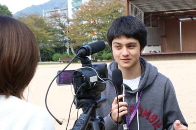 カメラを向けられマイクを持って答えているスクイムの男子生徒の写真