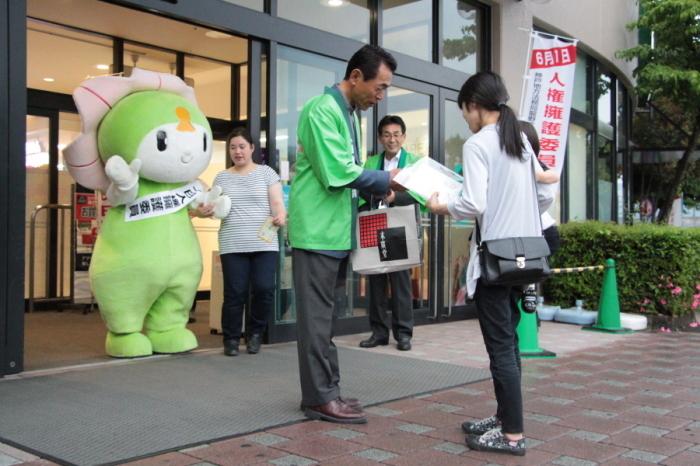 宍粟市ご当地キャラクターと緑色の法被をきた男性が施設の入り口で通行人に人権擁護の説明をしている写真