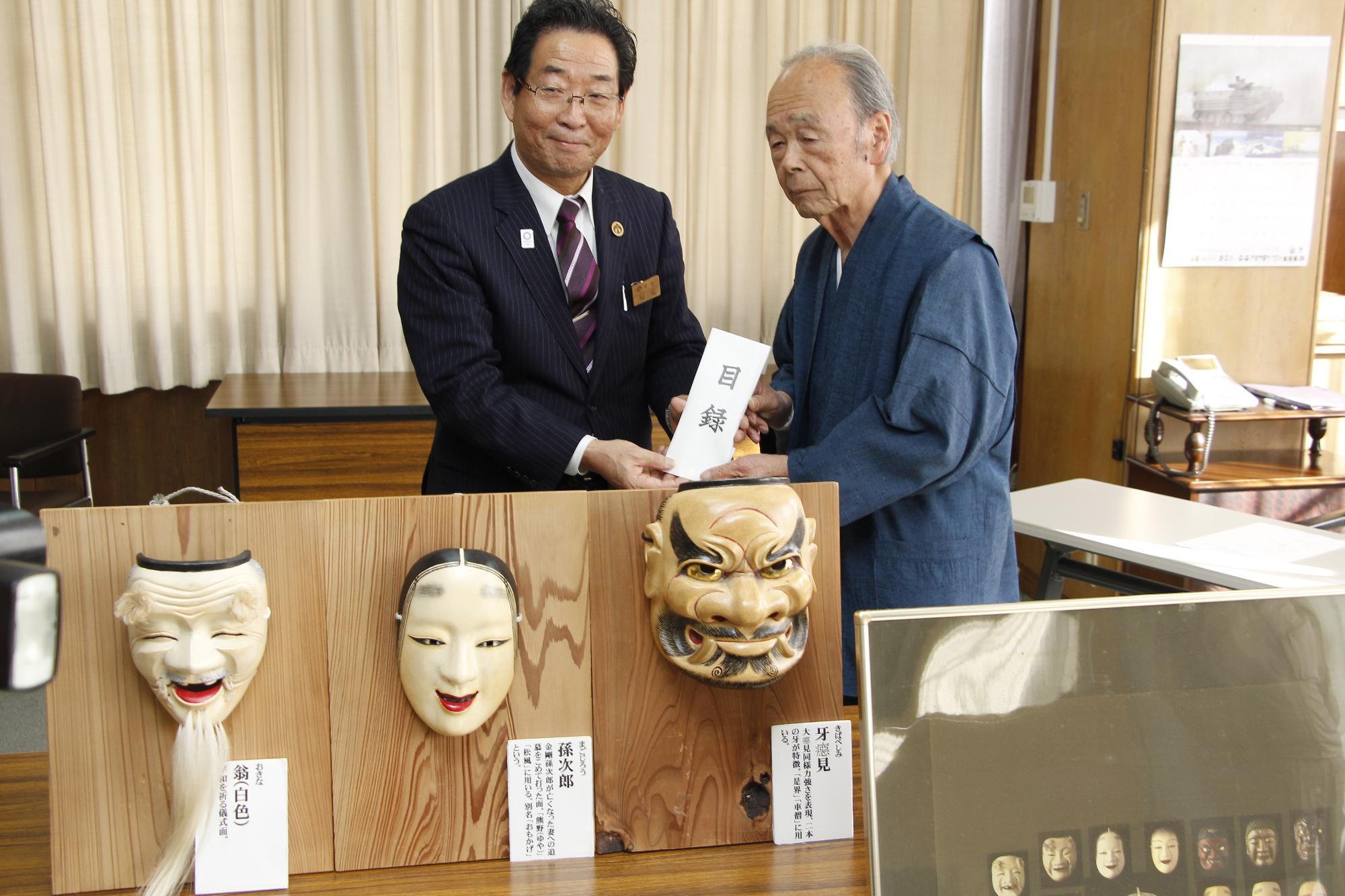 寄贈された能面と作務衣を着た作者と市長が写る記念写真
