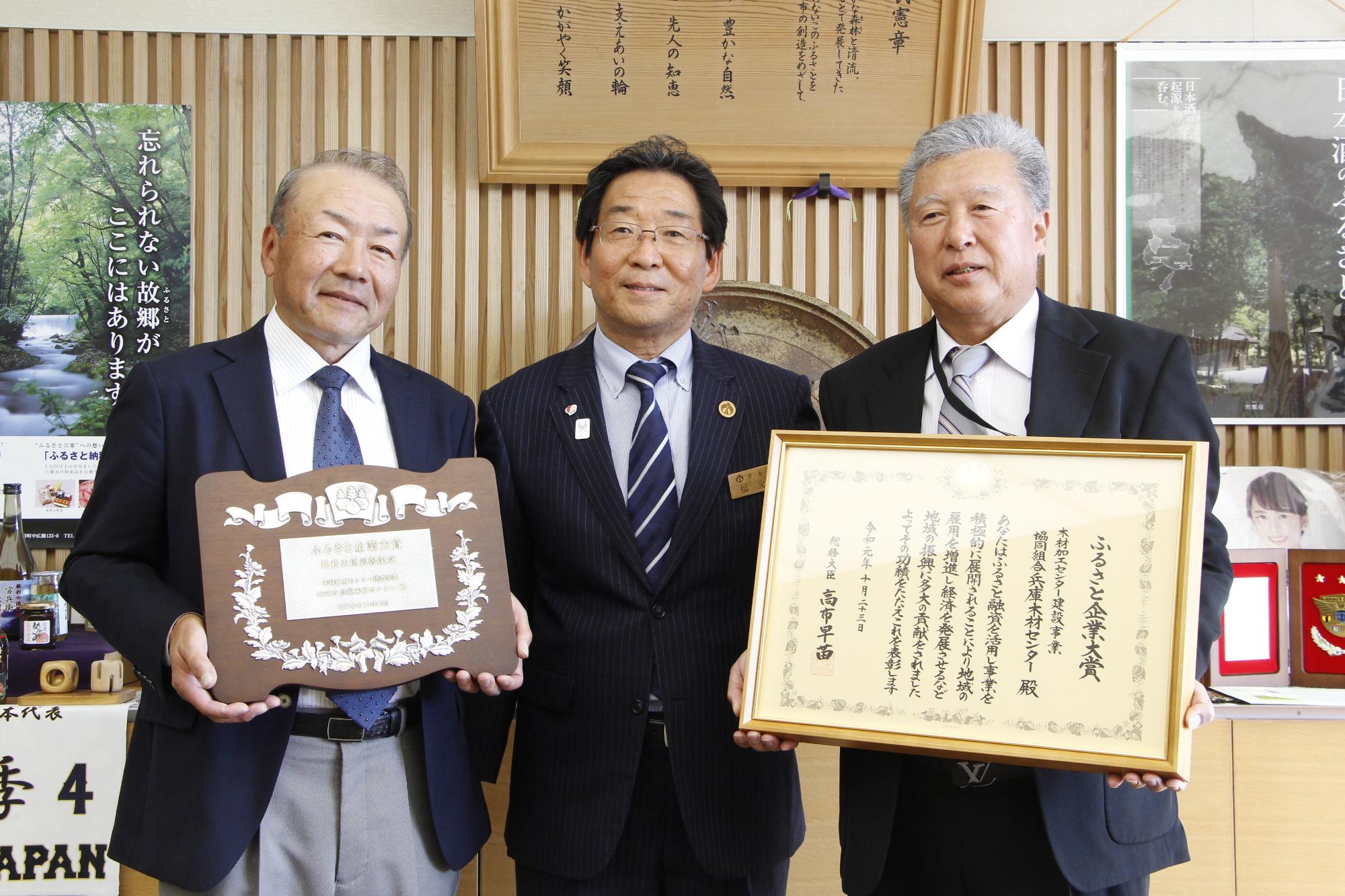表彰状と盾を持った木材センター役員二人と市長が並んでいる写真