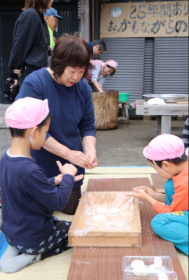 ついた餅を粉を付け丸めている園児2人の写真