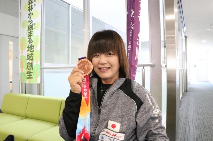 銅メダルを顔の横に持ち笑顔で写る西家さんの写真