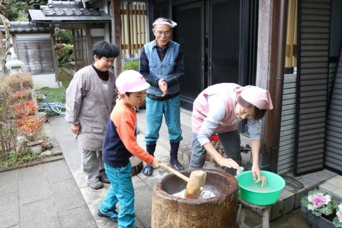 玄関の前で男児が杵を使い餅をつき、小田さんが餅を返している写真