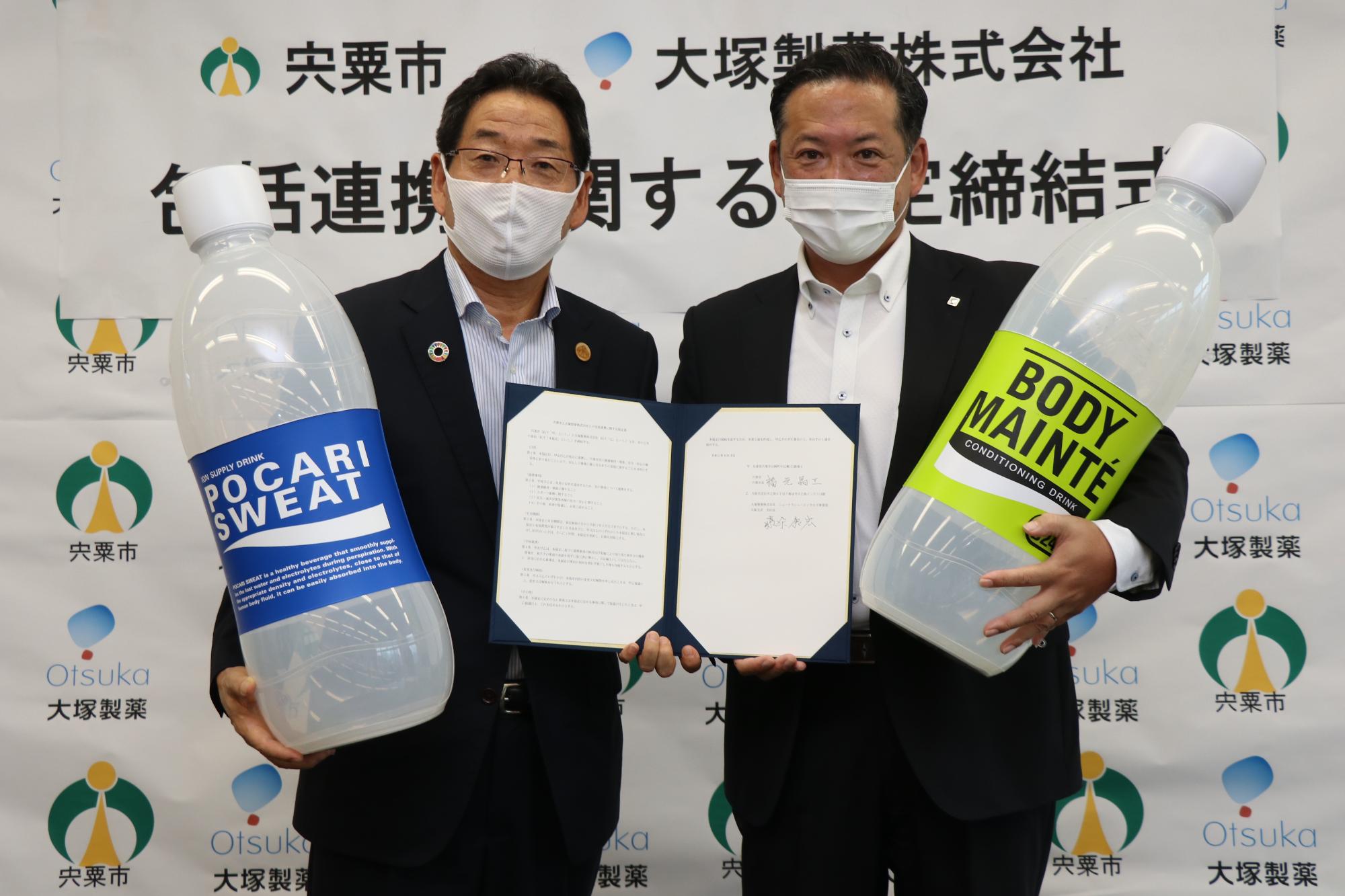 協定書を持つ福元市長と大塚製薬の大阪支店長藤原康宏さんが大きなポカリスエットの模型などを持って並んでいる写真