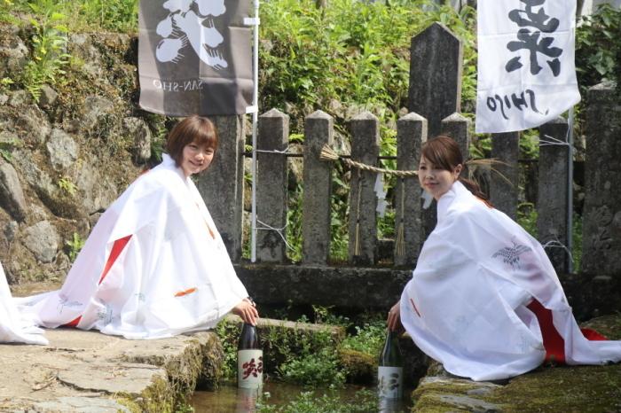 神社の境内に流れてる小川で二人の巫女さんが瓶に入った三笑を冷やしている写真
