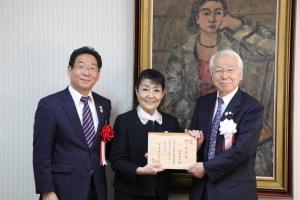 特任対しに任命された任命状を手にもつ今井さんと2人のスーツ姿の男性の記念写真