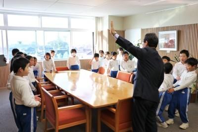 市長室でテーブルを囲んだ小学生たちに左手を上げて話しかける市長の写真