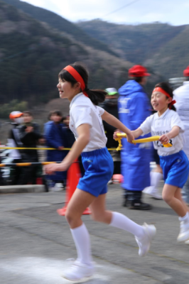 黄色いたすきを次の走者へ笑顔で渡す女子学生と前を見て走り出している次の走者の写真
