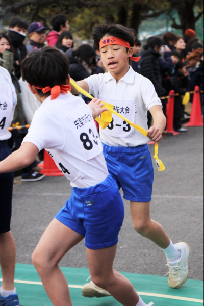 黄色いたすきを付きの走者へ渡す瞬間の男子学生と受け取る直前から走り出している走者の写真