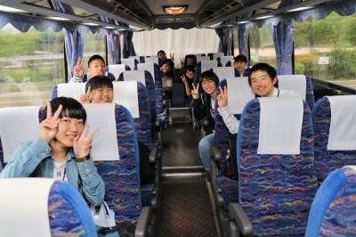 バスの中でカメラに向かってピースサインをする中学生たちの写真
