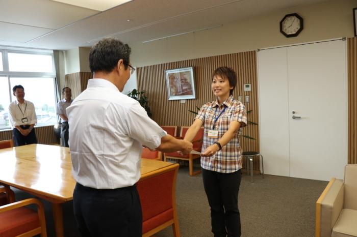 茶色い短髪の加藤智子さんが退任式で市長から賞状を受け取っている写真