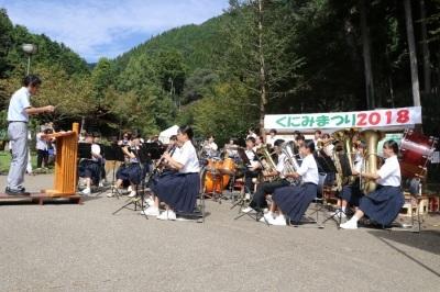 「くにみまつり2018」の横断幕の前で演奏している山崎南中学校吹奏楽部の写真