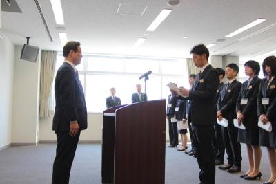 市役所辞令交付式で出席者の前にたち市長に対してスピーチを行っているスーツ姿の若い男性の写真